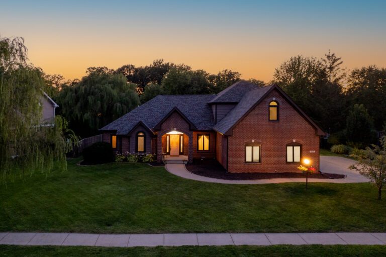 Aerial view of the front of a home at twilight with the windows glowing.