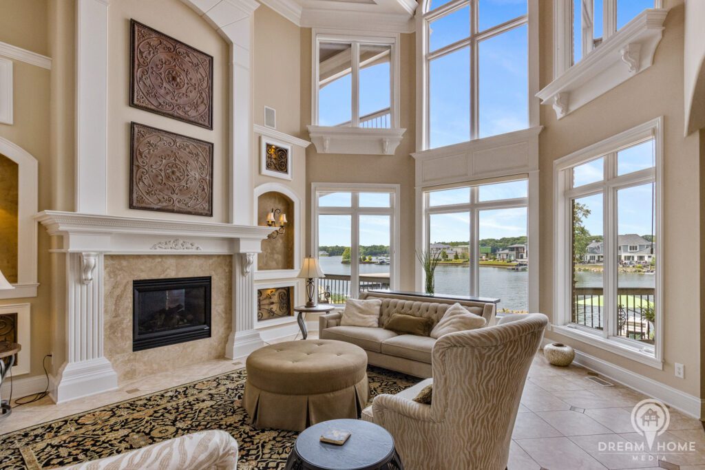 A great room of a luxury home with 2-story ceilings, fireplace and wall of windows looking out on a lake.